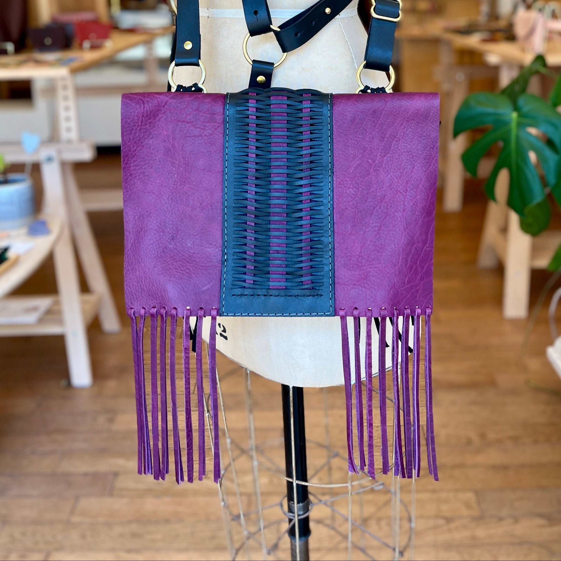 Purple handbag with black accents and fringe on a mannequin in a store setting.